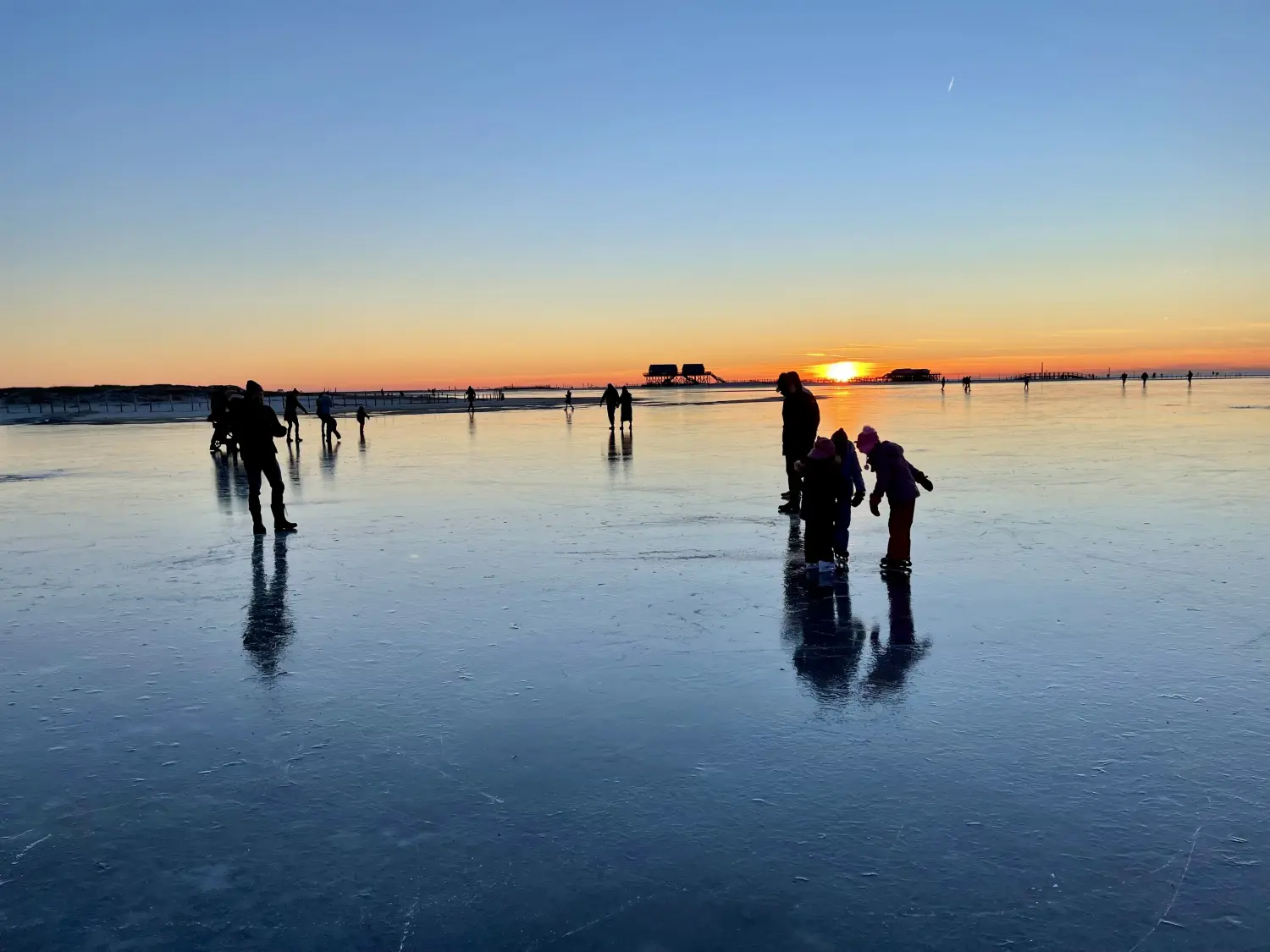 Eisiger Strand bei Sonnenuntergang mit Pfahlbauten in der Ferne