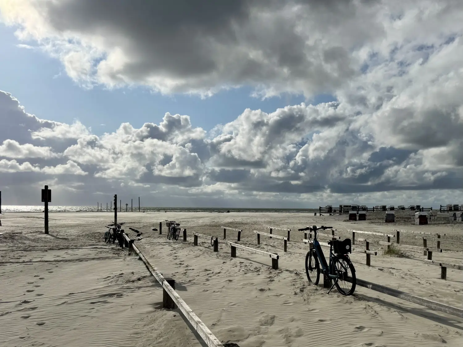 Mietfahrräder am Strandzaun in St. Peter-Ording unter großen Wolken
